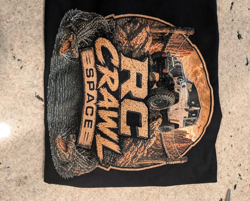 Black T-shirt laid flat with a large full-color RC Crawl Space back print featuring an off-road truck.